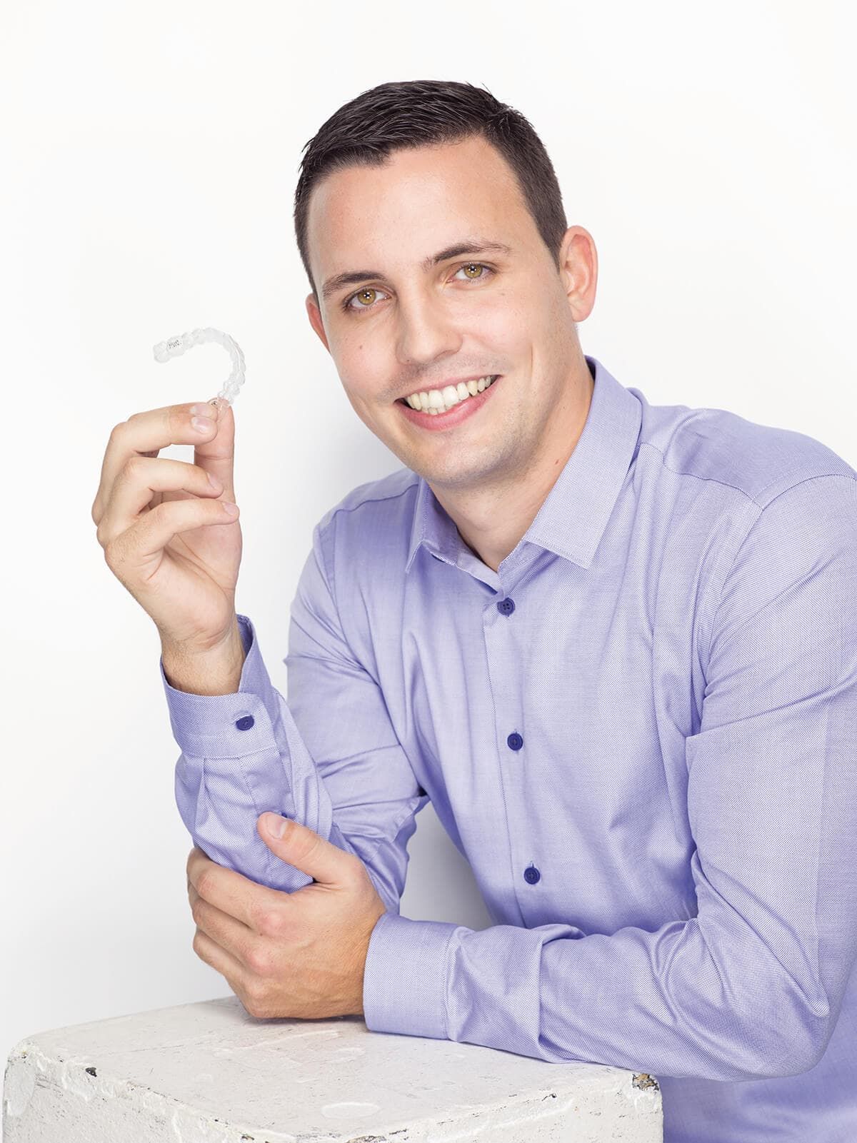 Man holding a dental aligner, smiling.