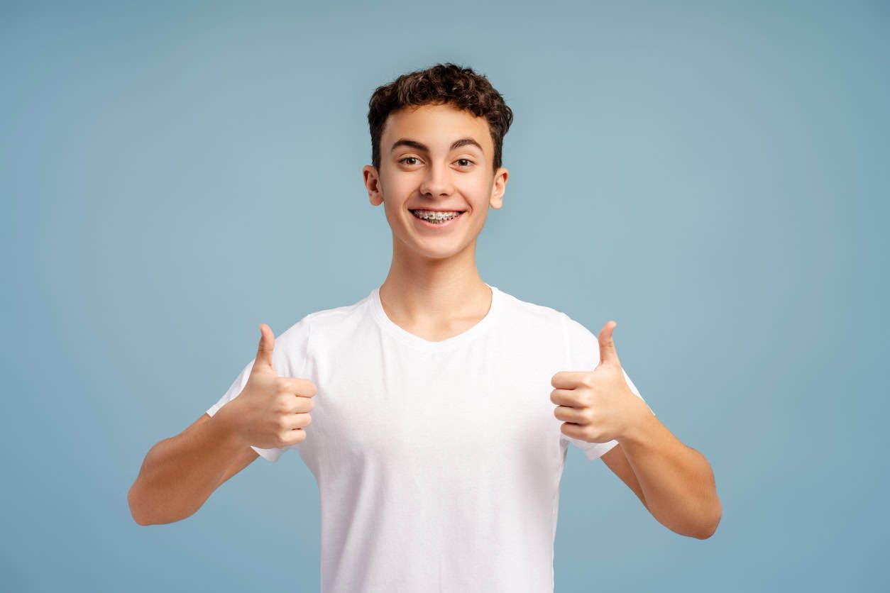 Smiling boy with braces giving thumbs up.